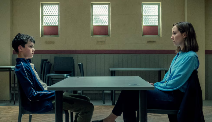 Cena da série Adolescência mostra a psicóloga Briony Ariston frente a frente com Jamie Miller, jovem investigado por homicídio, em um ambiente austero que representa a formalidade e a neutralidade da entrevista forense.