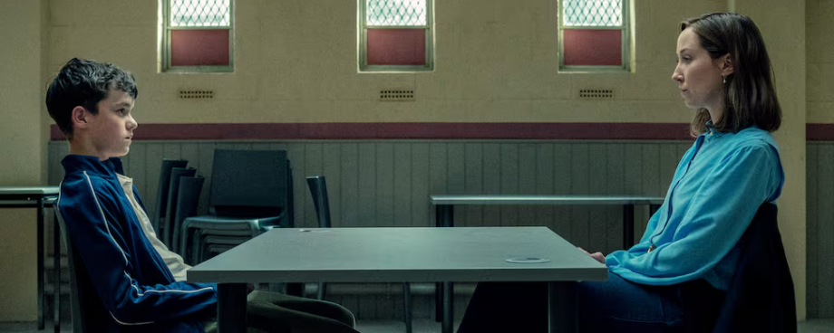 Cena da série Adolescência mostra a psicóloga Briony Ariston frente a frente com Jamie Miller, jovem investigado por homicídio, em um ambiente austero que representa a formalidade e a neutralidade da entrevista forense.