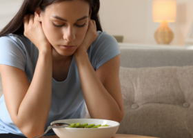 Mulher jovem demonstrando preocupação diante de um prato de salada, ilustrando a relação entre emoções e comportamento alimentar.