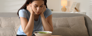 Mulher jovem demonstrando preocupação diante de um prato de salada, ilustrando a relação entre emoções e comportamento alimentar.