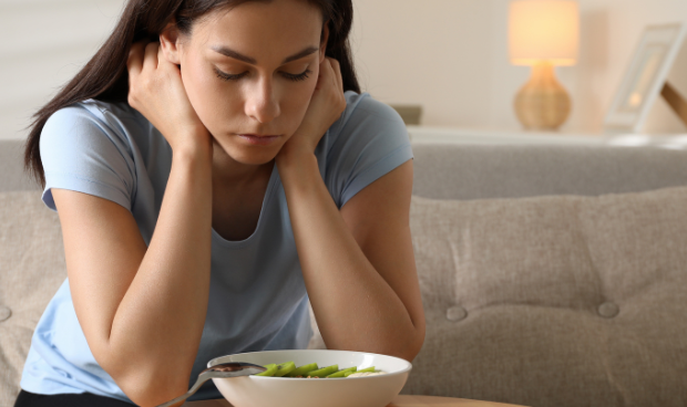 Mulher jovem demonstrando preocupação diante de um prato de salada, ilustrando a relação entre emoções e comportamento alimentar.