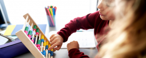 Criança em atividade de estímulo cognitivo usando ábaco colorido, durante prática educativa alinhada à abordagem ABA