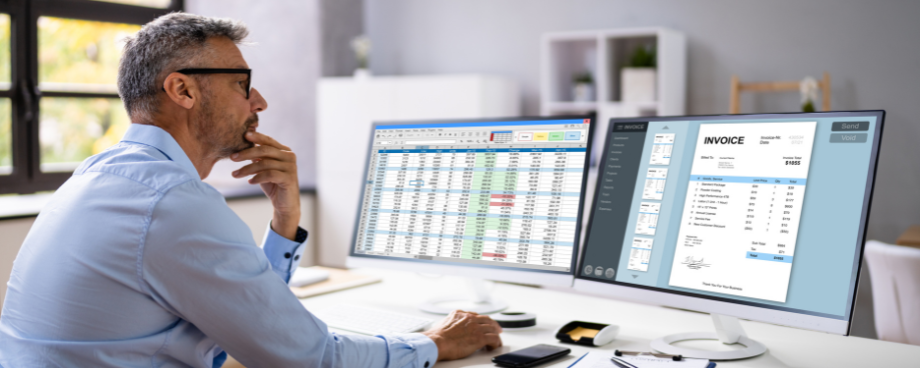 Homem analisa planilhas e documentos fiscais em dois monitores, representando a importância do planejamento e gestão tributária.