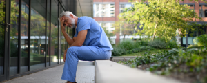 Médico exausto sentado do lado de fora do hospital, com expressão de cansaço e mãos na cabeça, simbolizando os efeitos do burnout na medicina e a importância de soluções como a Inteligência Artificial para reduzir a sobrecarga profissional.