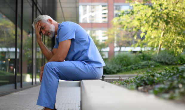 Médico exausto sentado do lado de fora do hospital, com expressão de cansaço e mãos na cabeça, simbolizando os efeitos do burnout na medicina e a importância de soluções como a Inteligência Artificial para reduzir a sobrecarga profissional.