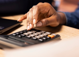 Profissional realiza cálculos em calculadora ao lado de notebook, representando rotinas de compliance fiscal e controle tributário no contexto da Reforma Tributária.