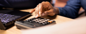 Profissional realiza cálculos em calculadora ao lado de notebook, representando rotinas de compliance fiscal e controle tributário no contexto da Reforma Tributária.