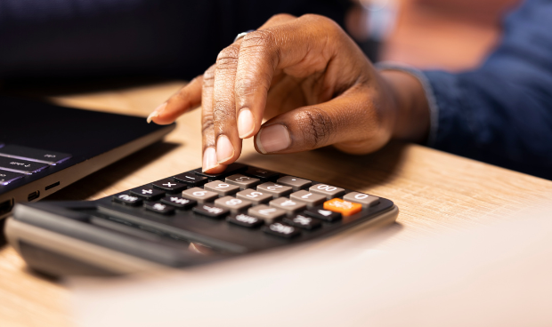 Profissional realiza cálculos em calculadora ao lado de notebook, representando rotinas de compliance fiscal e controle tributário no contexto da Reforma Tributária.